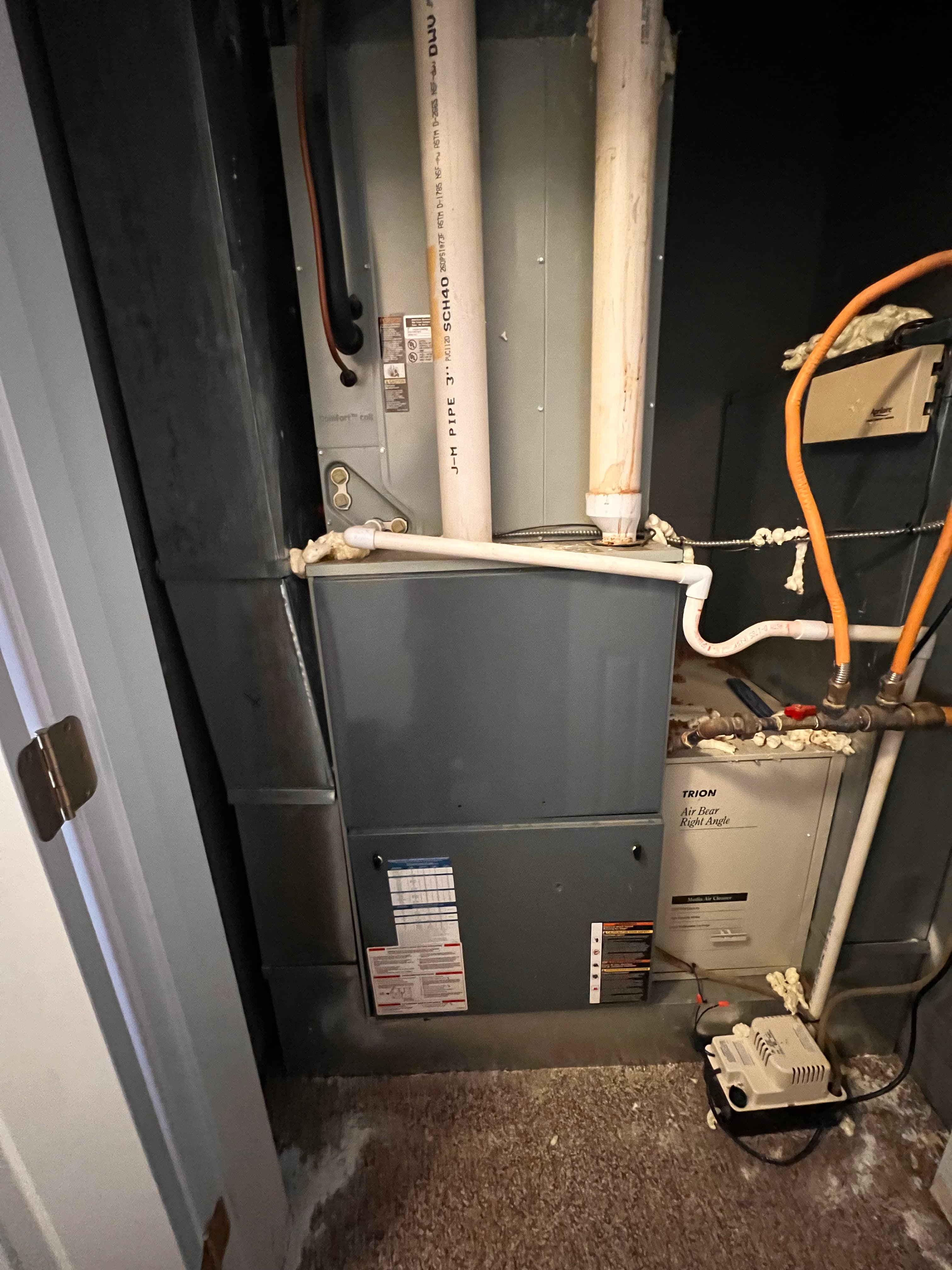Grey furnace unit with white PVC pipes and orange gas lines in a utility room.